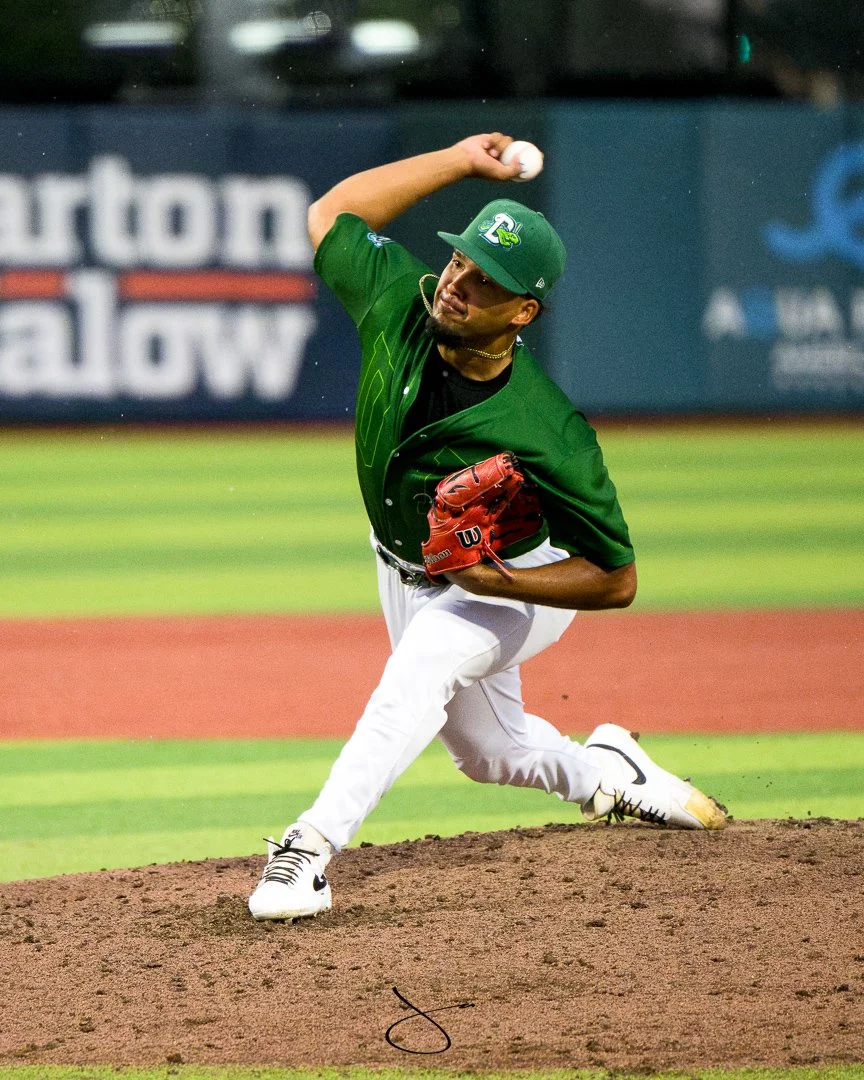 A baseball player in a green and white uniform pitching on the mound at a baseball stadium.
