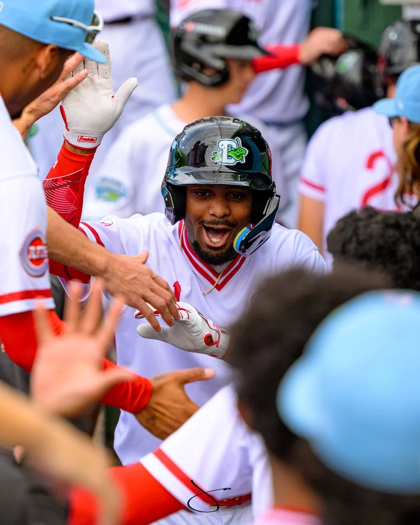 A baseball player with a helmet and gloves celebrating with teammates during a game.