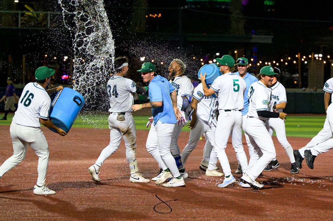 Group of baseball players celebrating on the field, some pouring water on each other, at night during a game.