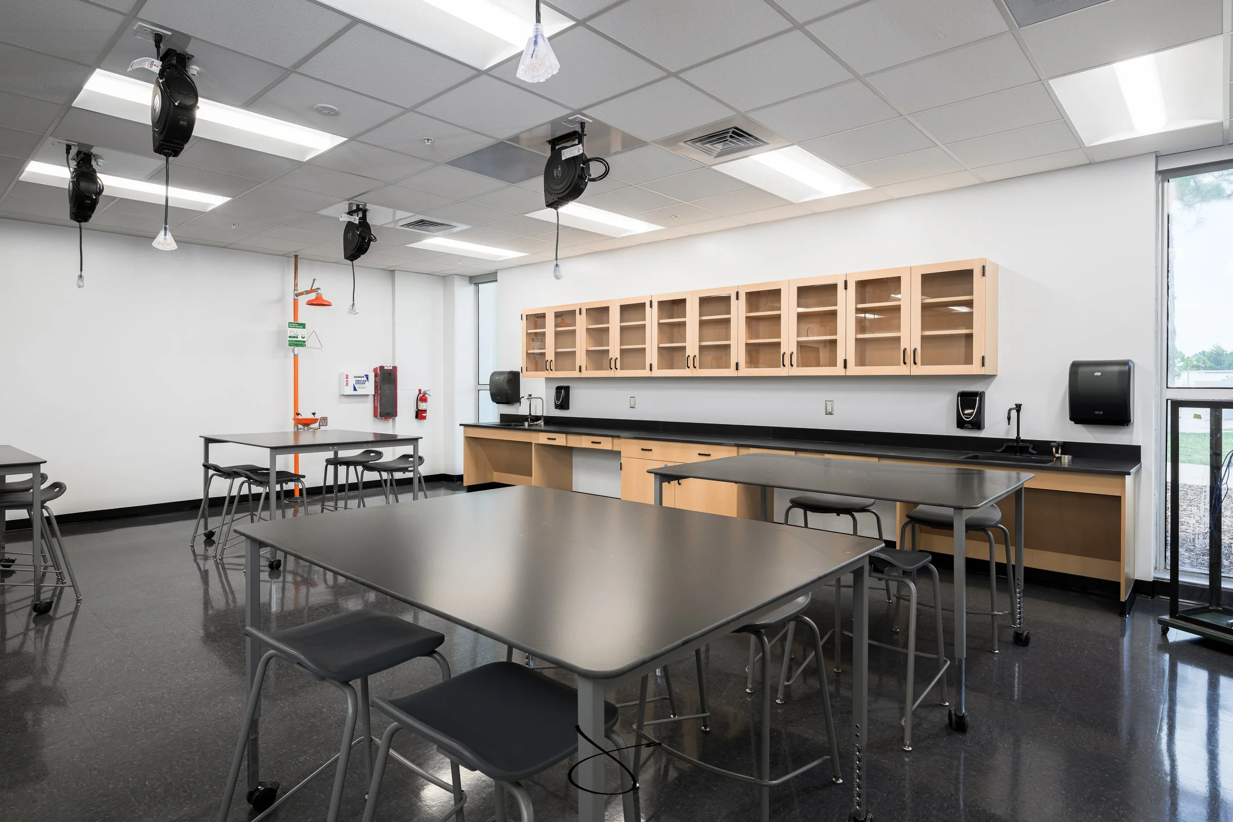 Empty classroom or laboratory with tables, chairs, cabinets, and medical or laboratory equipment, with source of natural light from a large window.
