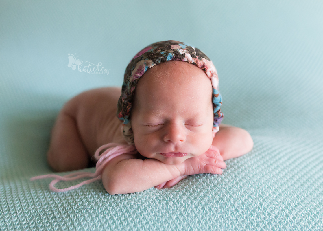 newborn baby twin girl wearing a floral bonnet lying on a blue blanket