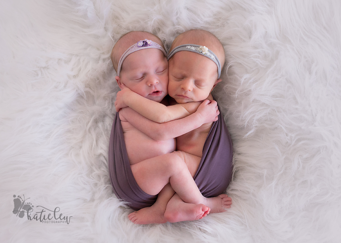 Twin baby girls hugging each other and wrapped in purple