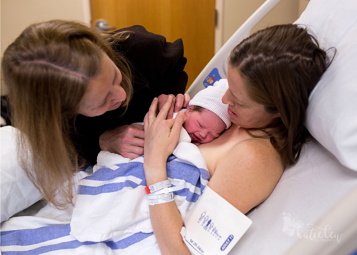 grandmother and mother admire newborn baby girl after her birth