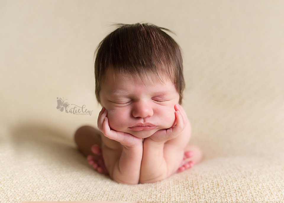 A baby girl resting in froggy pose on a creamy yellow backdrop