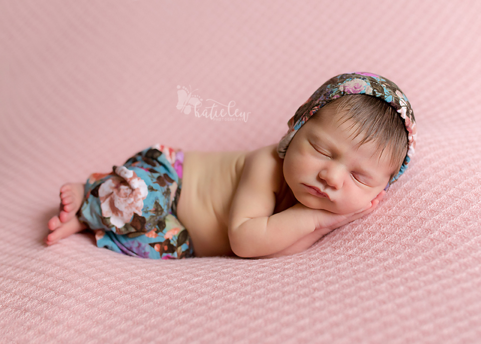 A baby girl wearing a blue floral outfit sleeping on a pink blanket