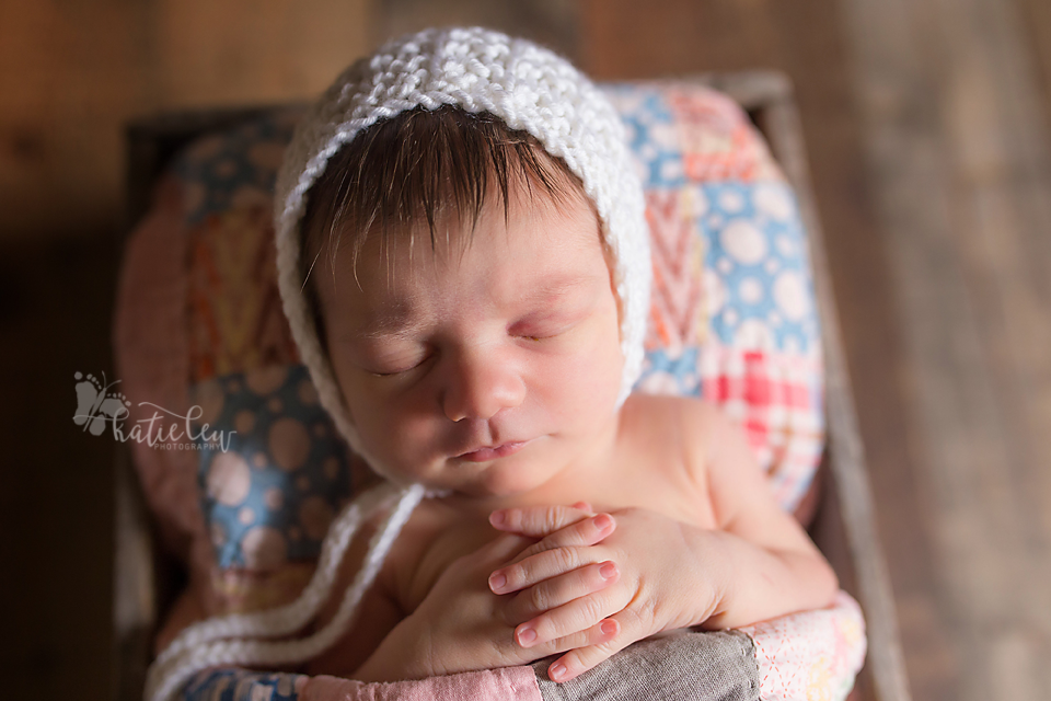 A sweet baby girl wearing a bonnet and laying in a bed.