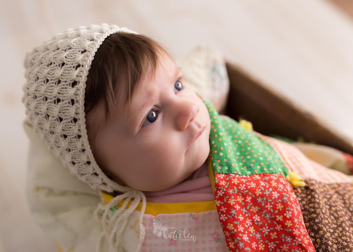 little baby wearing a bonnet and wrapped in a quilt.