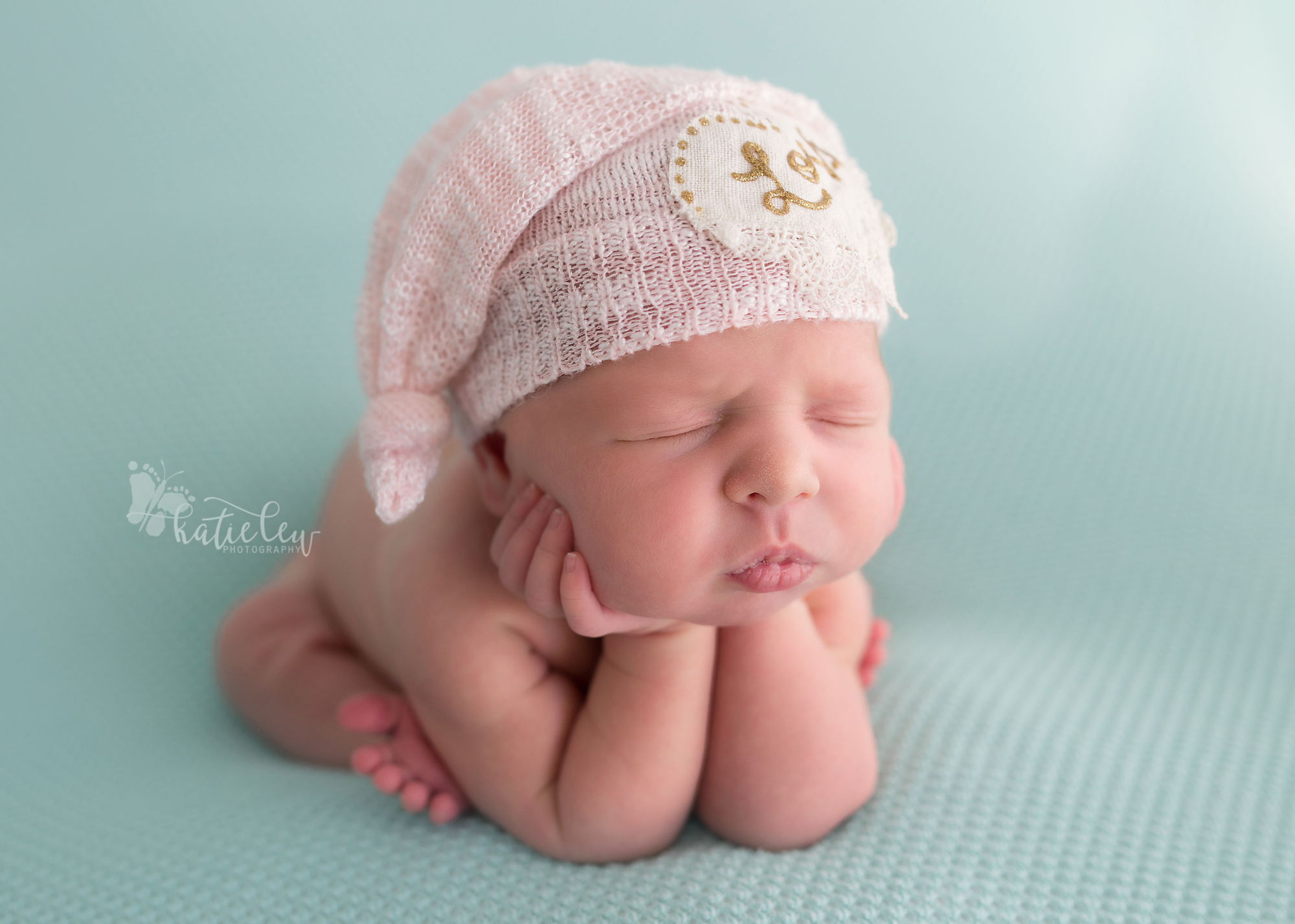 A side view of froggy pose with a baby girl wearing a pink hat.