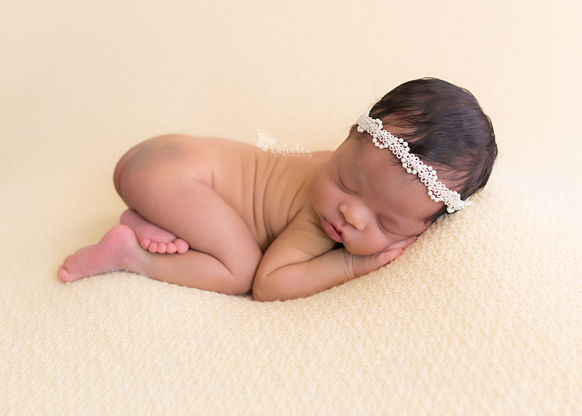 newborn wearing a pearl tieback on a creamy background