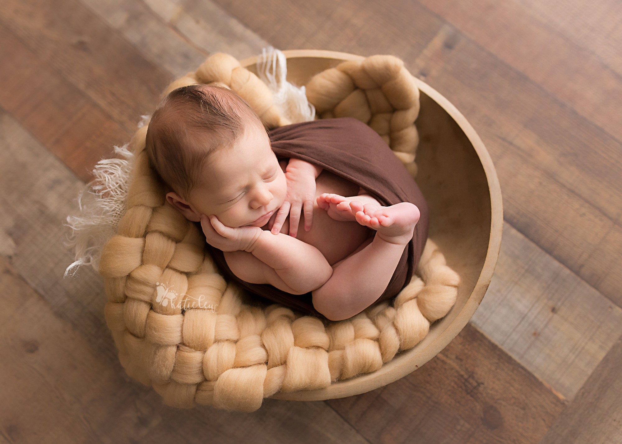 Natural newborn swaddled in brown and laid in a bowl.