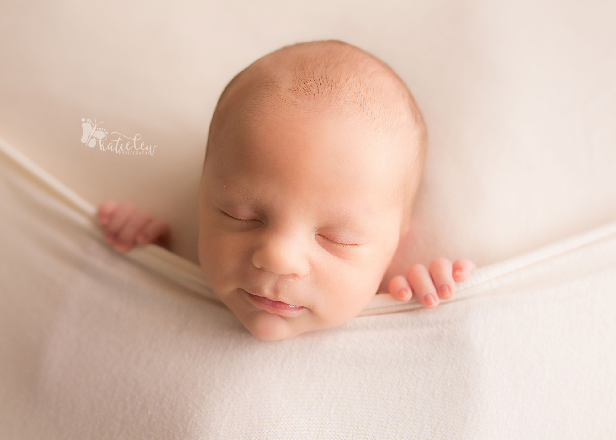 sweet newborn boy all tucked in against a cream background