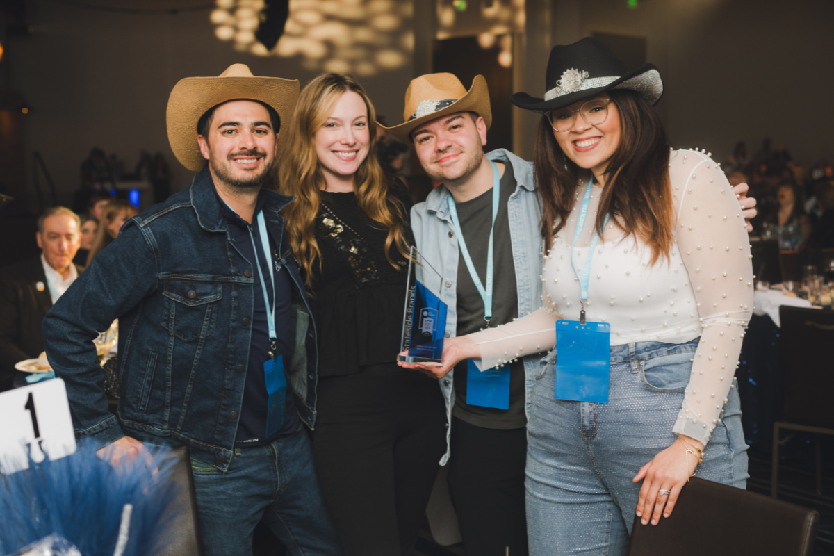 Group of four people wearing cowboy hats, smiling at an award ceremony, with one person holding a glass award.