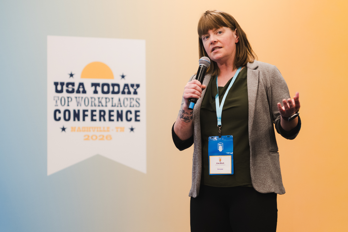 A woman speaking into a microphone at the USA Today Top Workplaces Conference in Nashville, Tennessee, 2020, standing near a sign with event details.