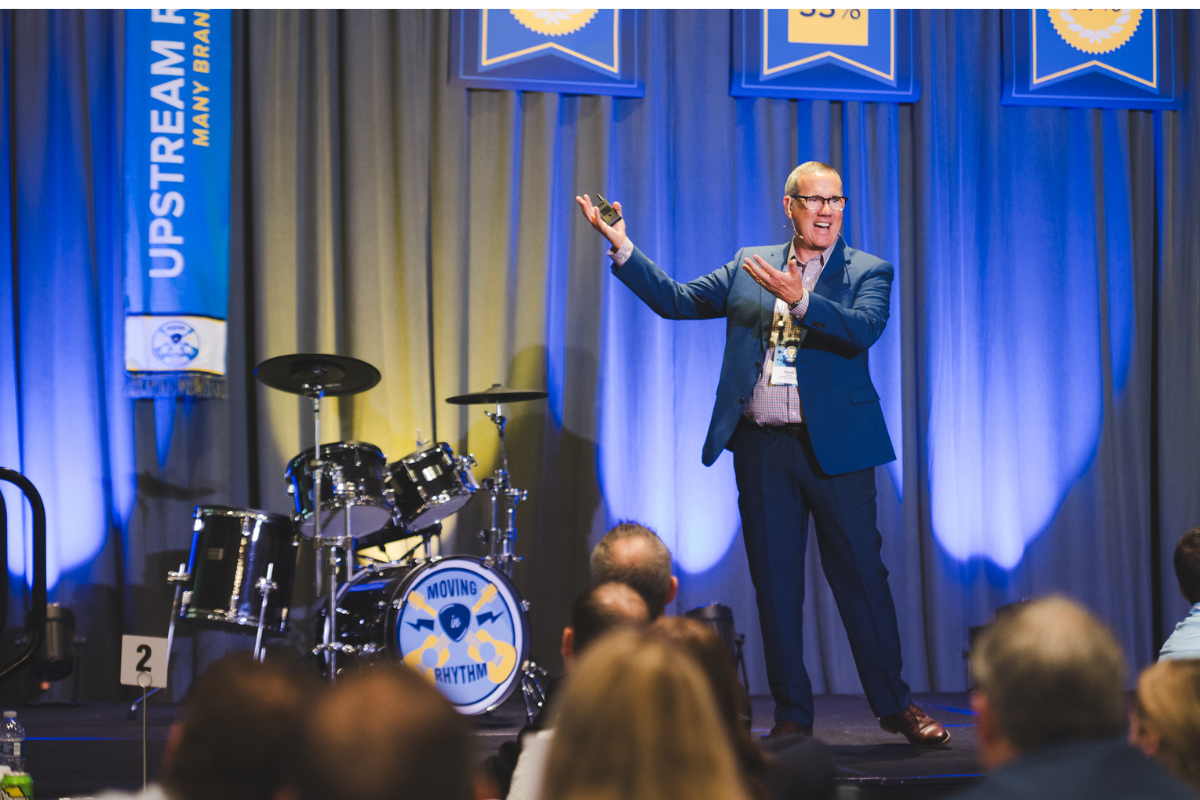 man on a stage in a blue suit gesturing his hands to his right while doing a presentation.