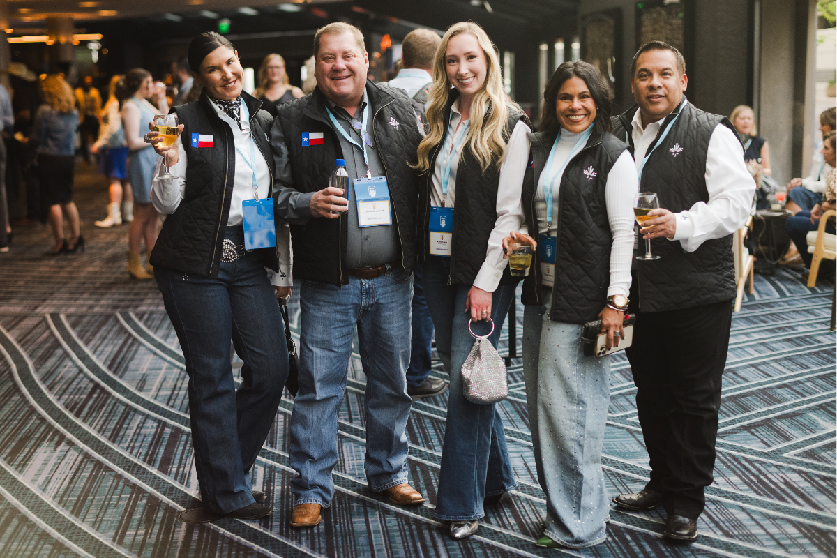 Group of five diverse people smiling and holding drinks at a social event or conference