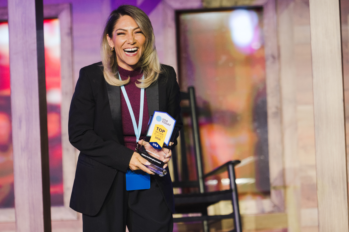 A woman holding an award trophy while smiling and laughing at an indoor event with colorful lighting and wooden decor.