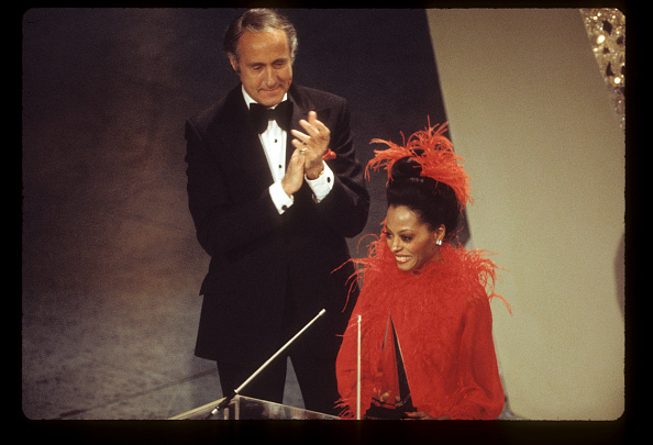 Diana Ross, in red ostrich trimmed cape, accepting an award from Henry Mancini at the American Music Awards on February 19, 1974. 