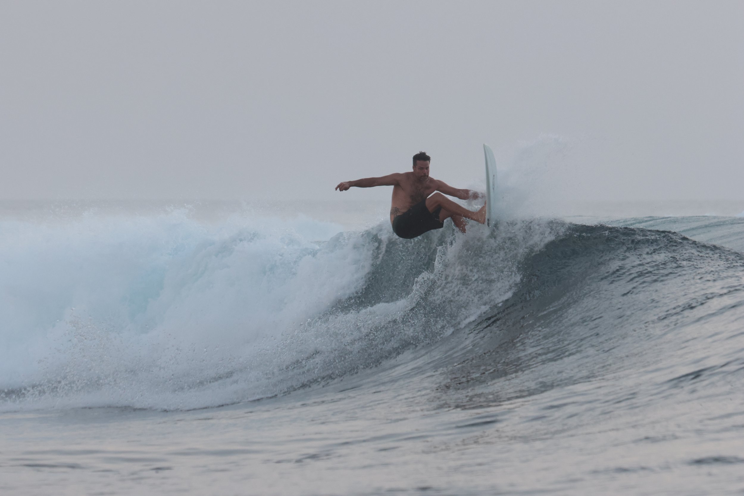 A shirtless man wearing black shorts surfing on a large wave in the ocean.