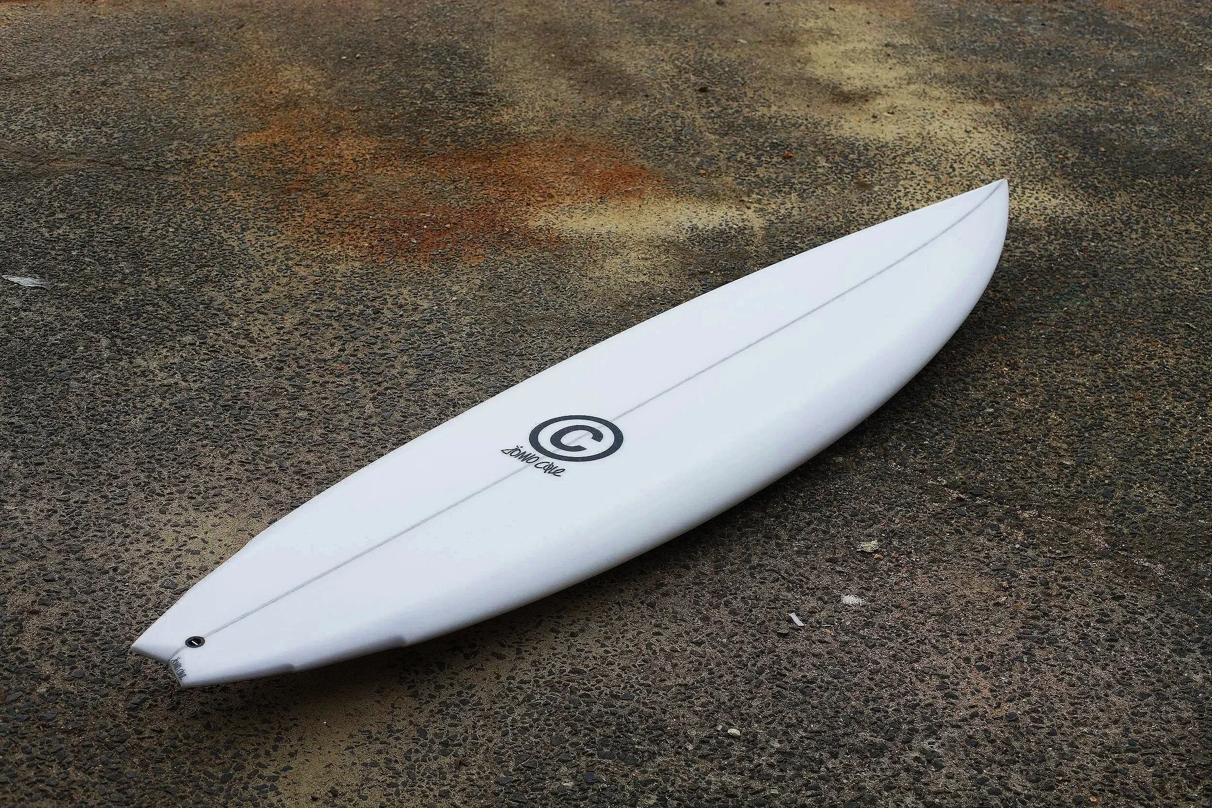 A white surfboard lying on a rough, textured brown surface outdoors