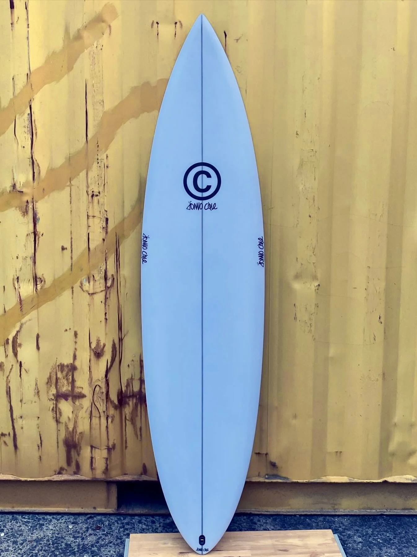 A light blue surfboard leaning against a yellow wooden wall.