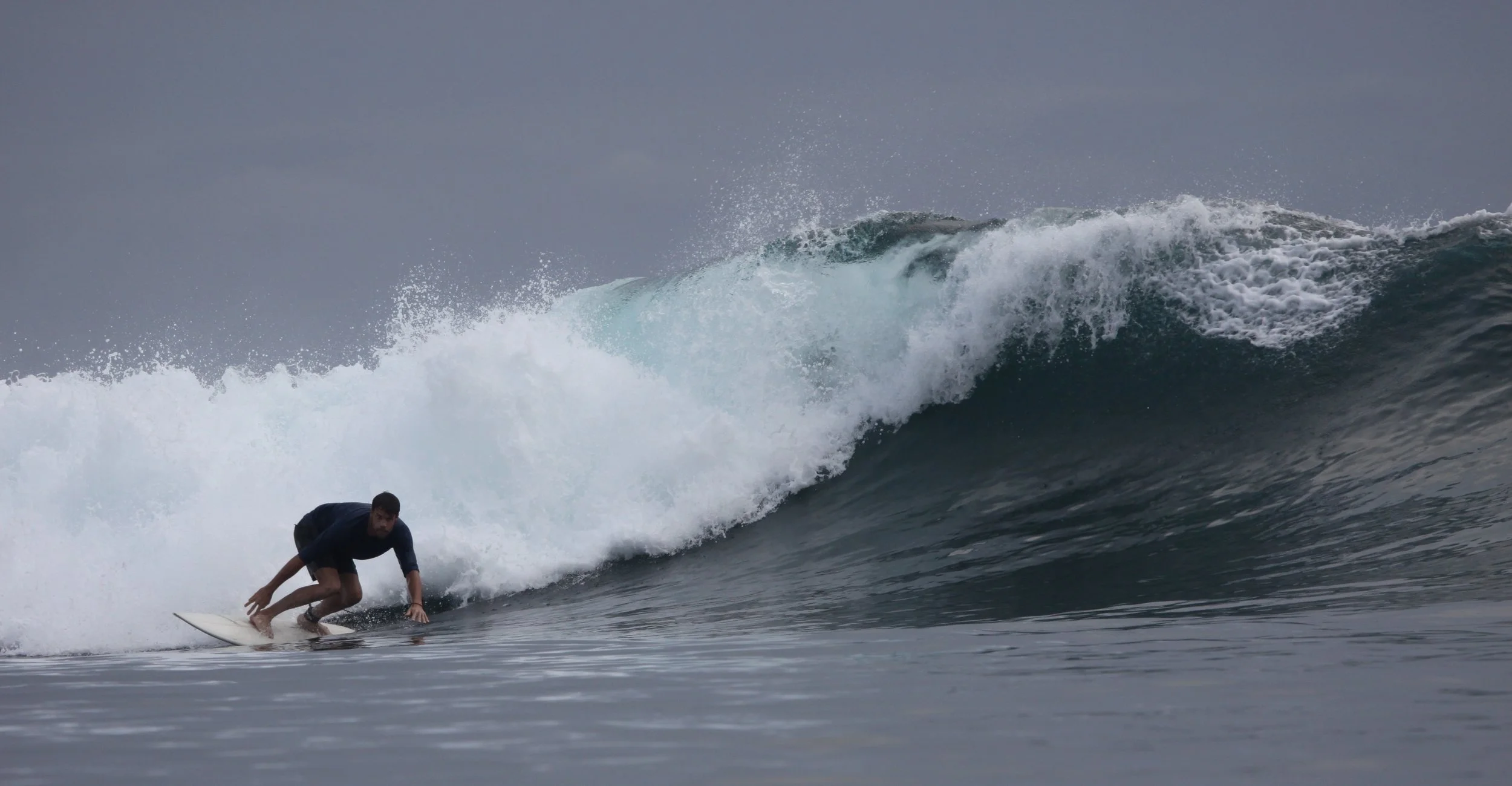 A man surfing on a large ocean wave under a cloudy sky.
