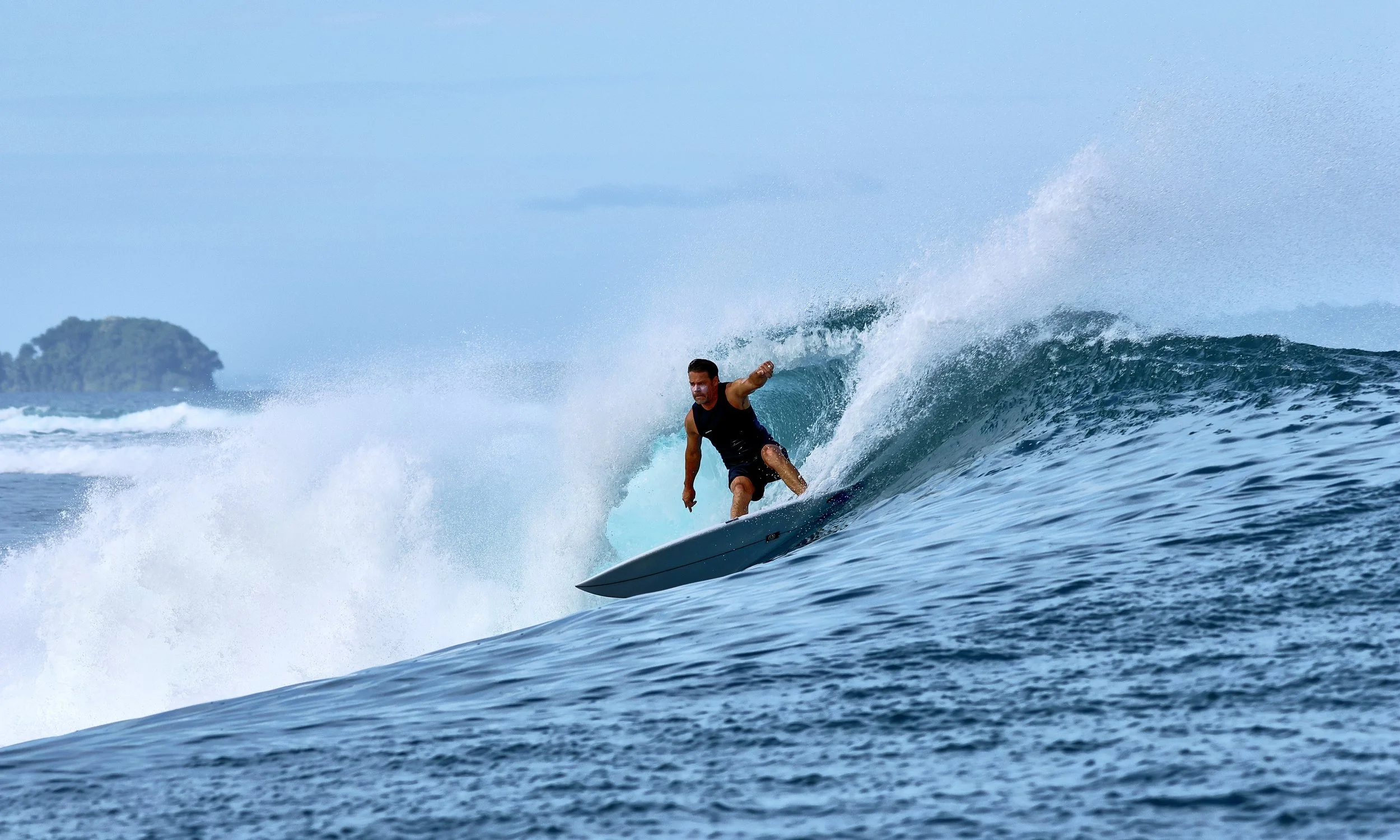 Man surfing on a wave in the ocean with an island in the background.