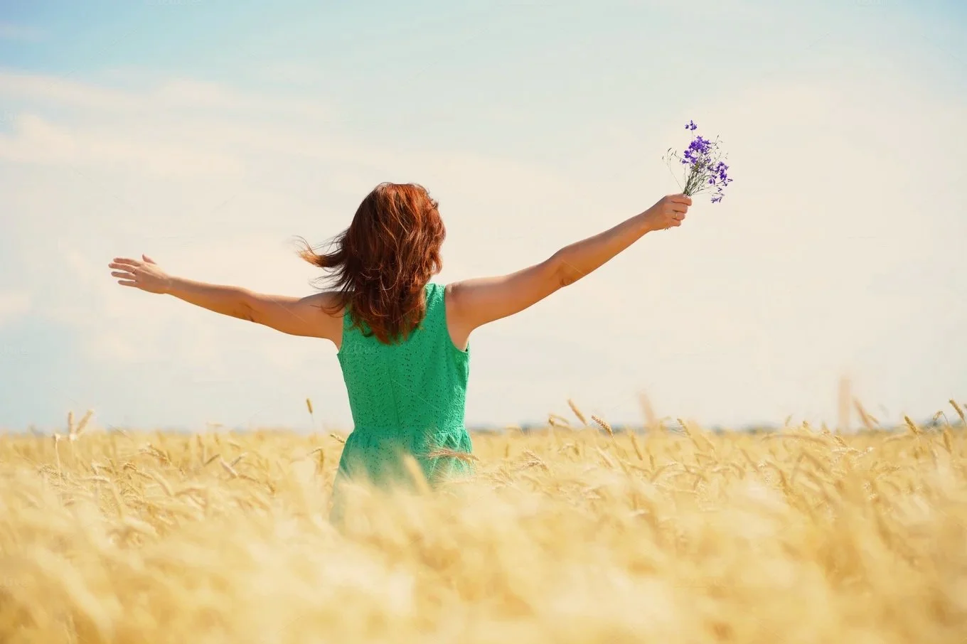 Woman standing in a field of wheat with arms spread and holding flowers