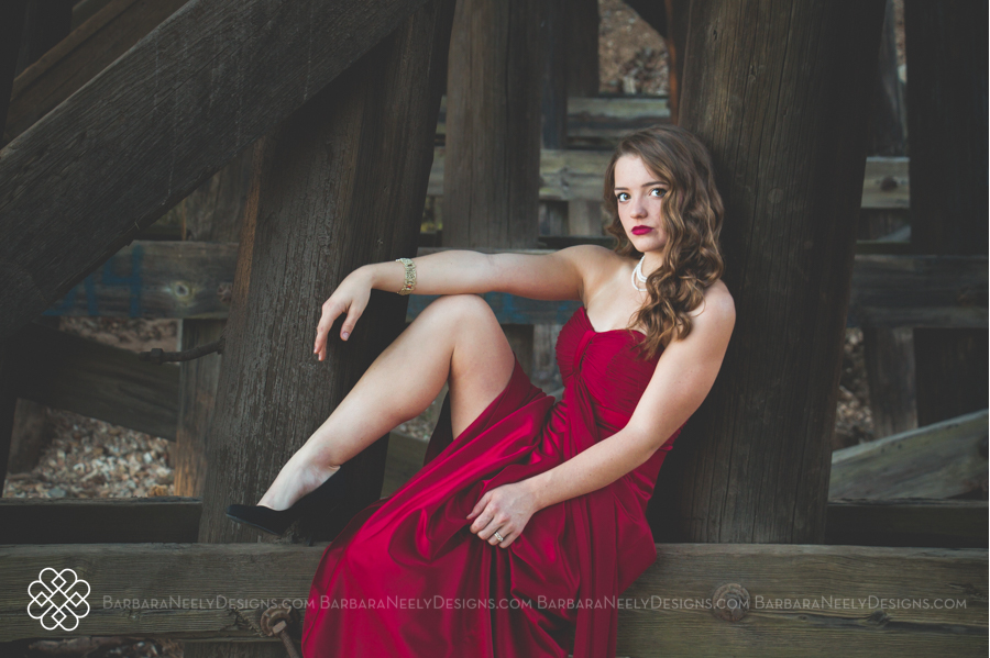 Very dramatic senior girl in red prom dress on railroad truss