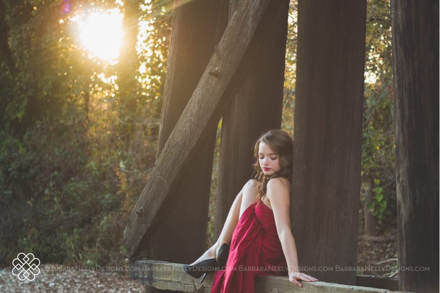 Very dramatic senior girl in red prom dress on railroad truss