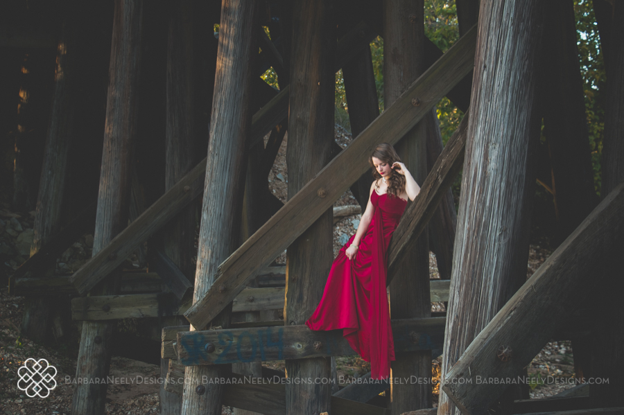 Very dramatic senior girl in red prom dress on railroad truss