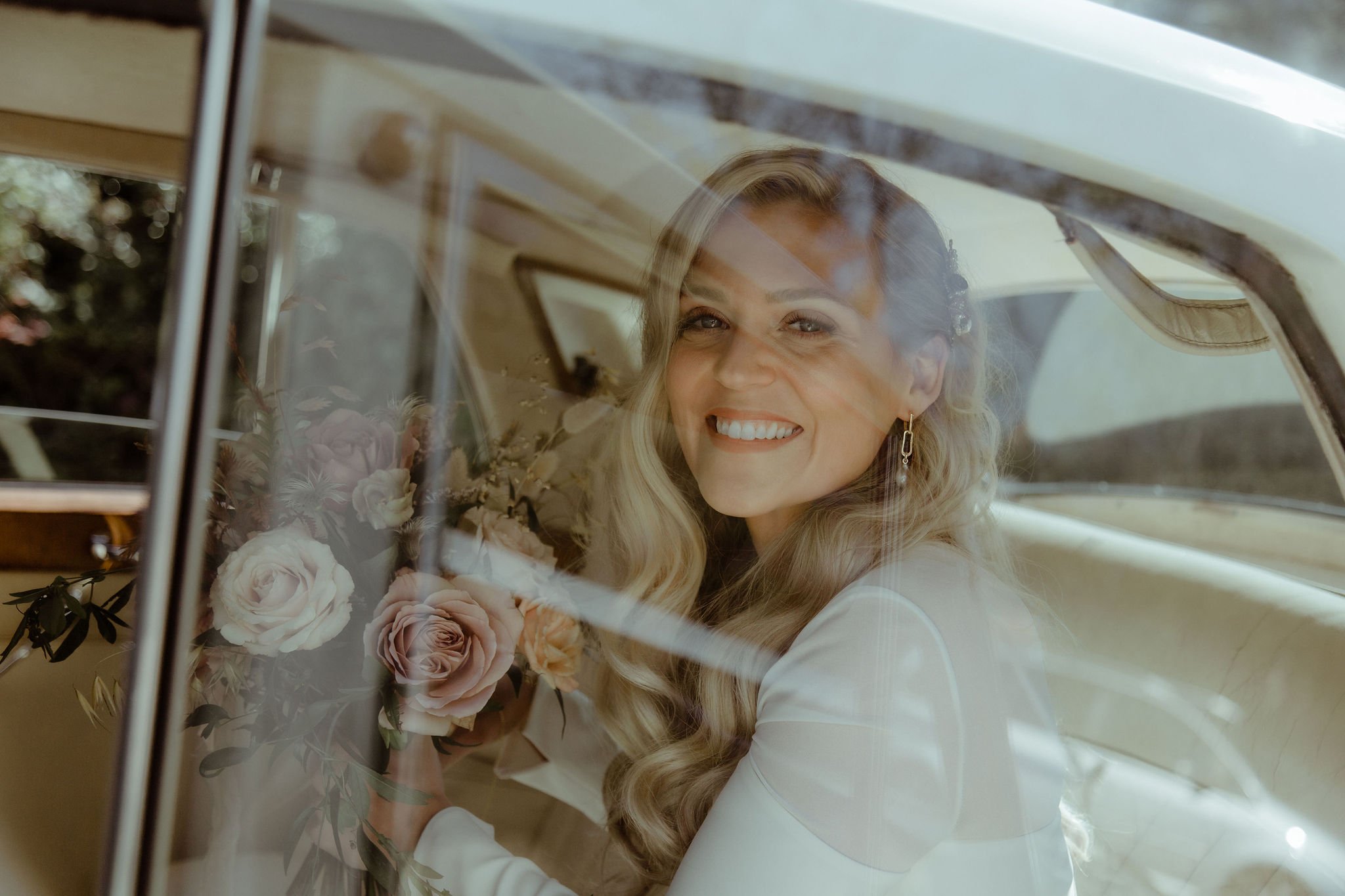 Smiling bride with muted elegant bouquet in cream wedding car