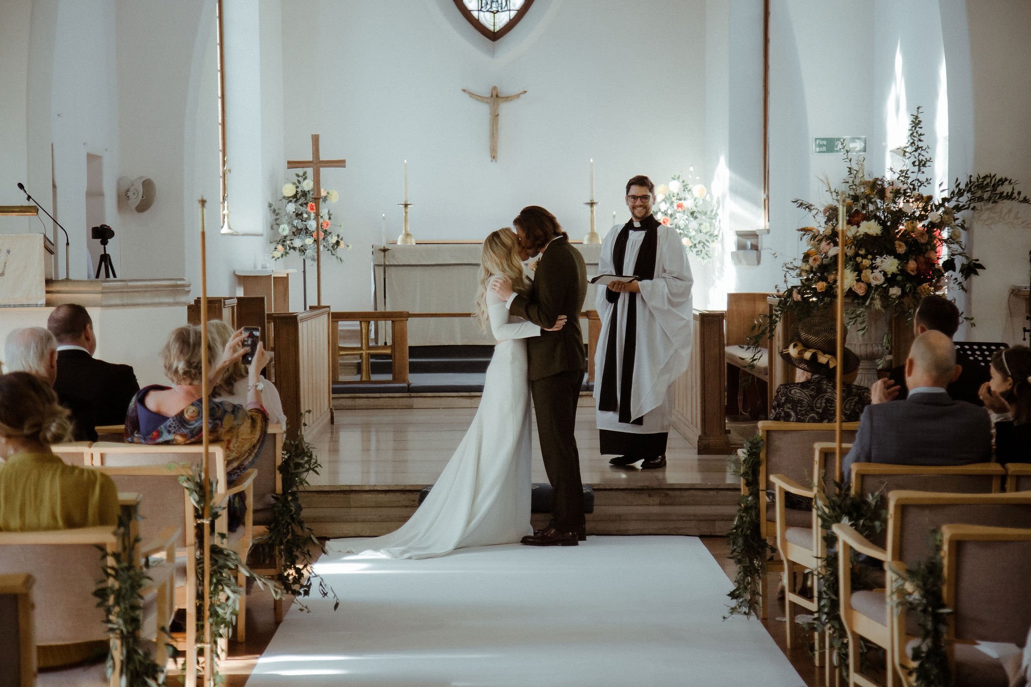 Bride and groom kiss at alter inside stunning white church by the seaside UK