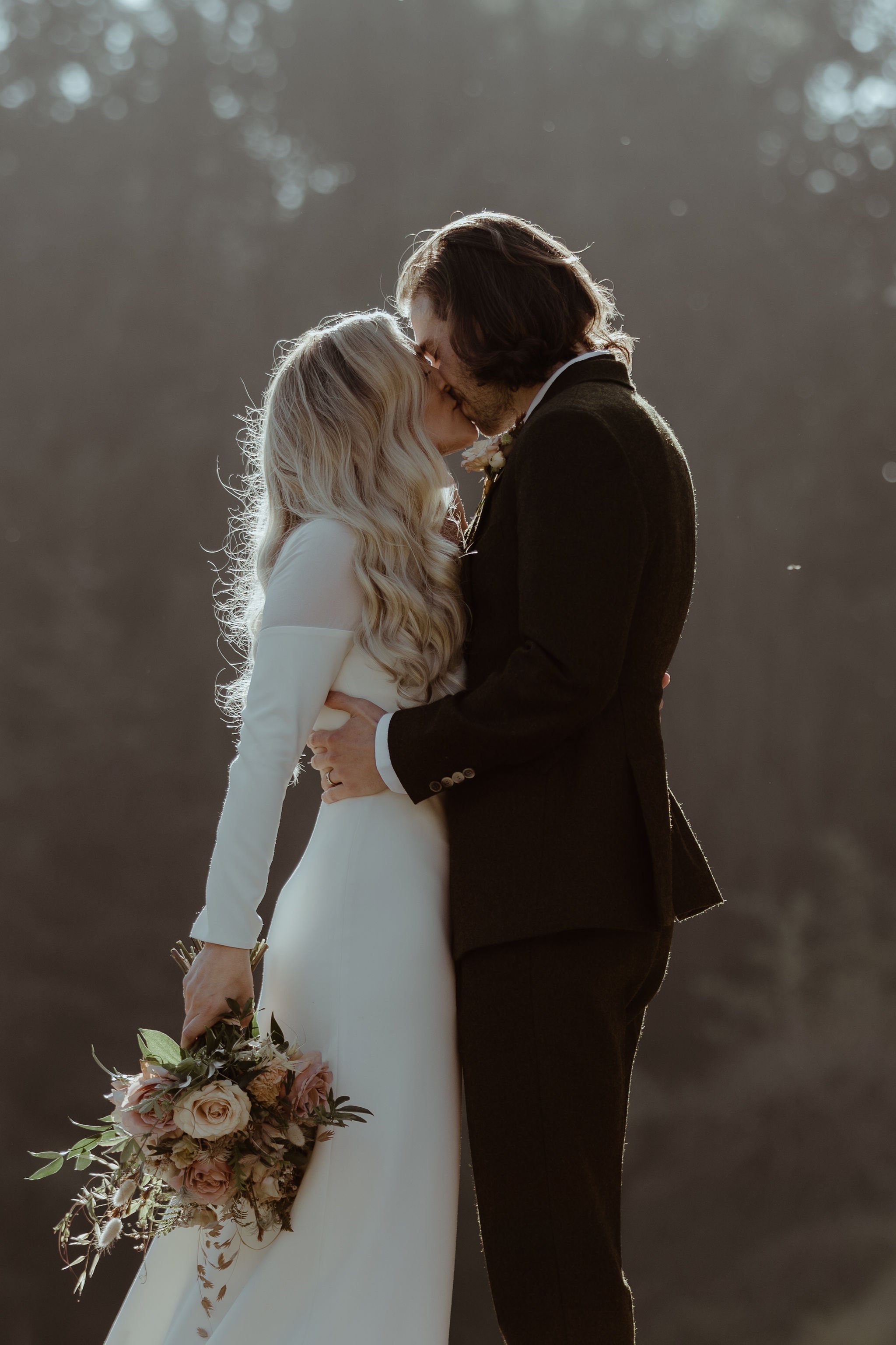 Bride wearing long sleeved winter wedding dress for UK October wedding with peach and pink bouquet 
