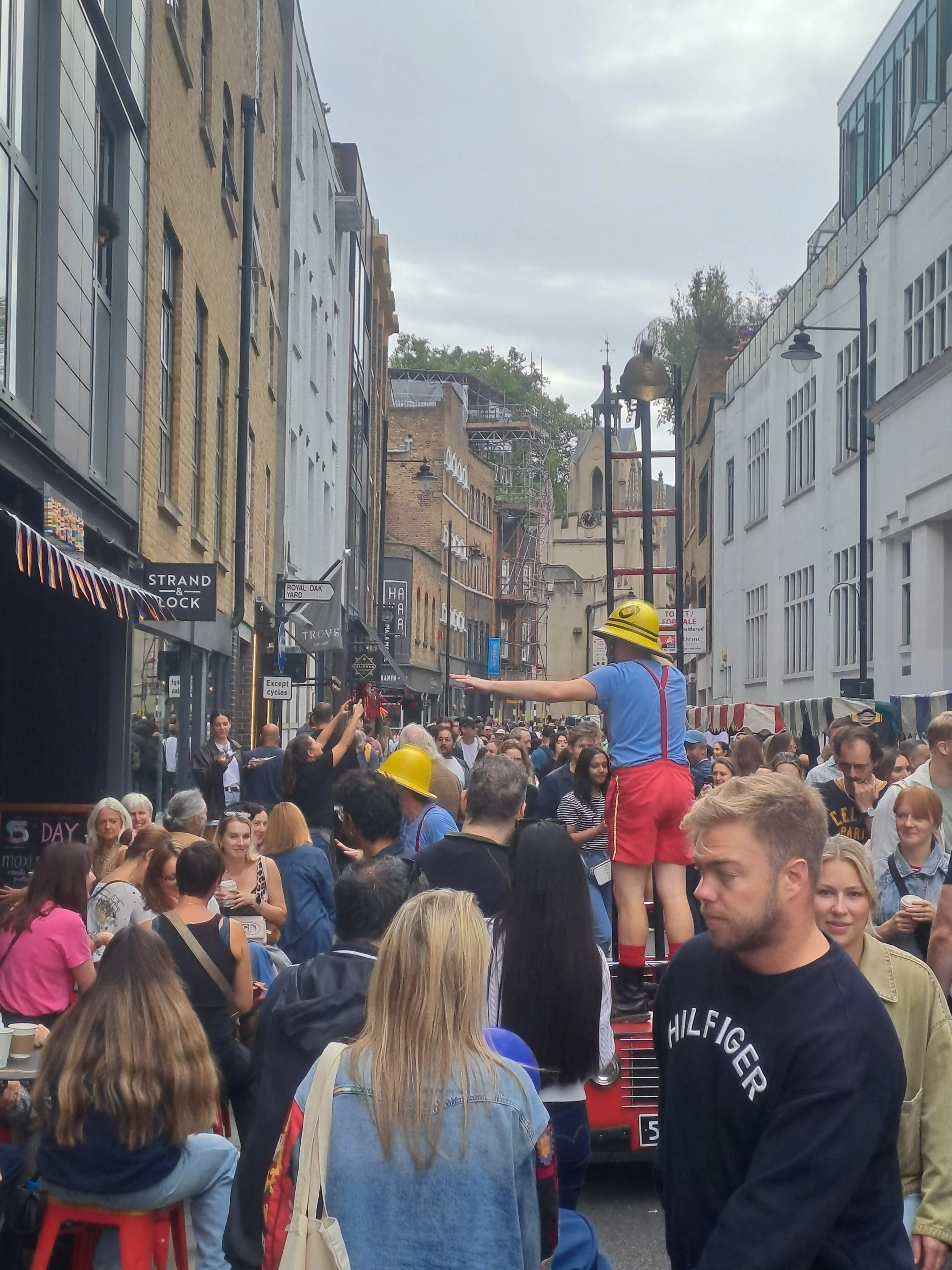 Bermondsey Street Festival photo taken 2025.  Lots of people enjoying the celebrations on the street with a street performer.  A great day out for all.