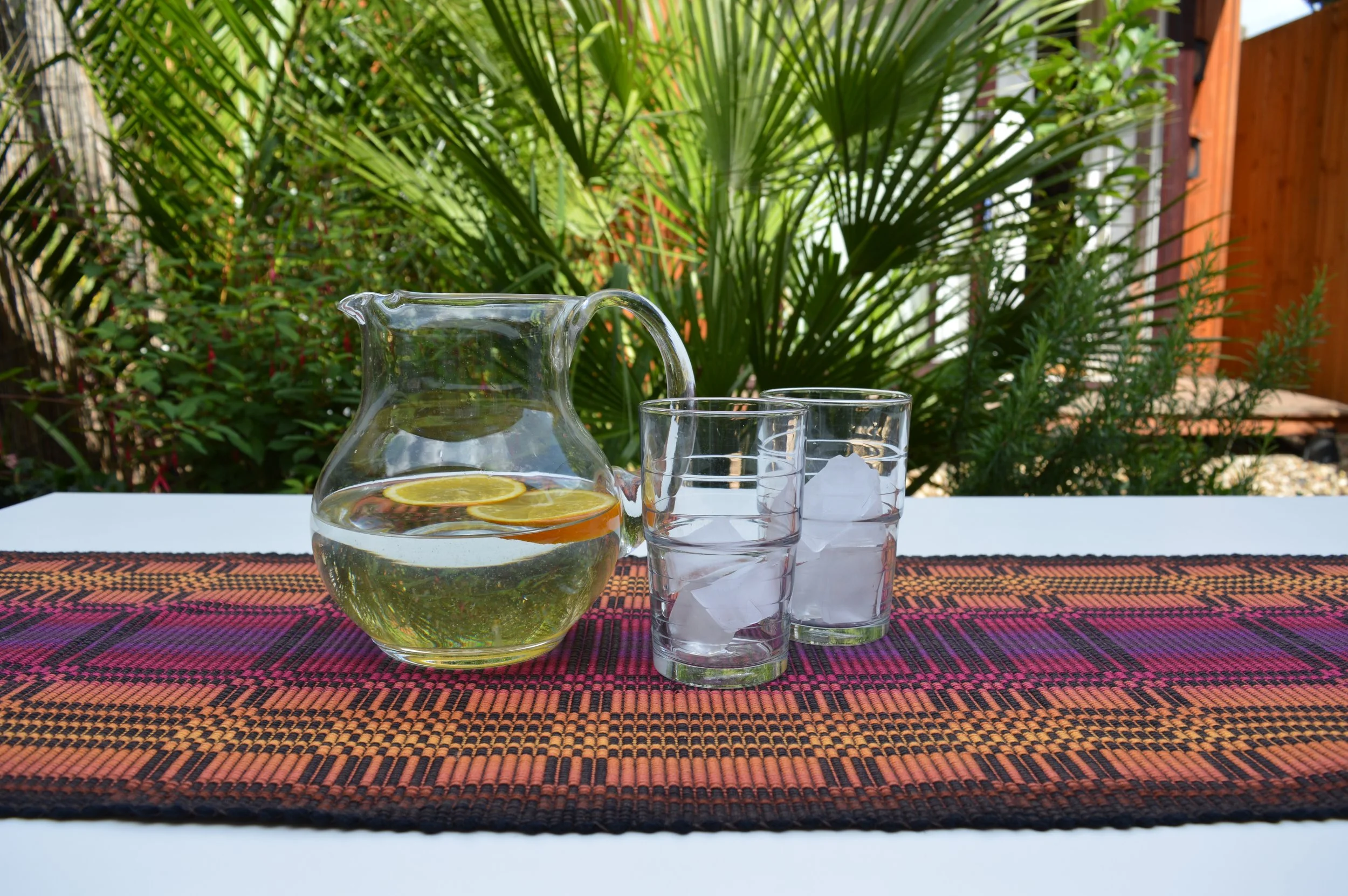 Table runner with jug and glasses. Backdrop garden view.