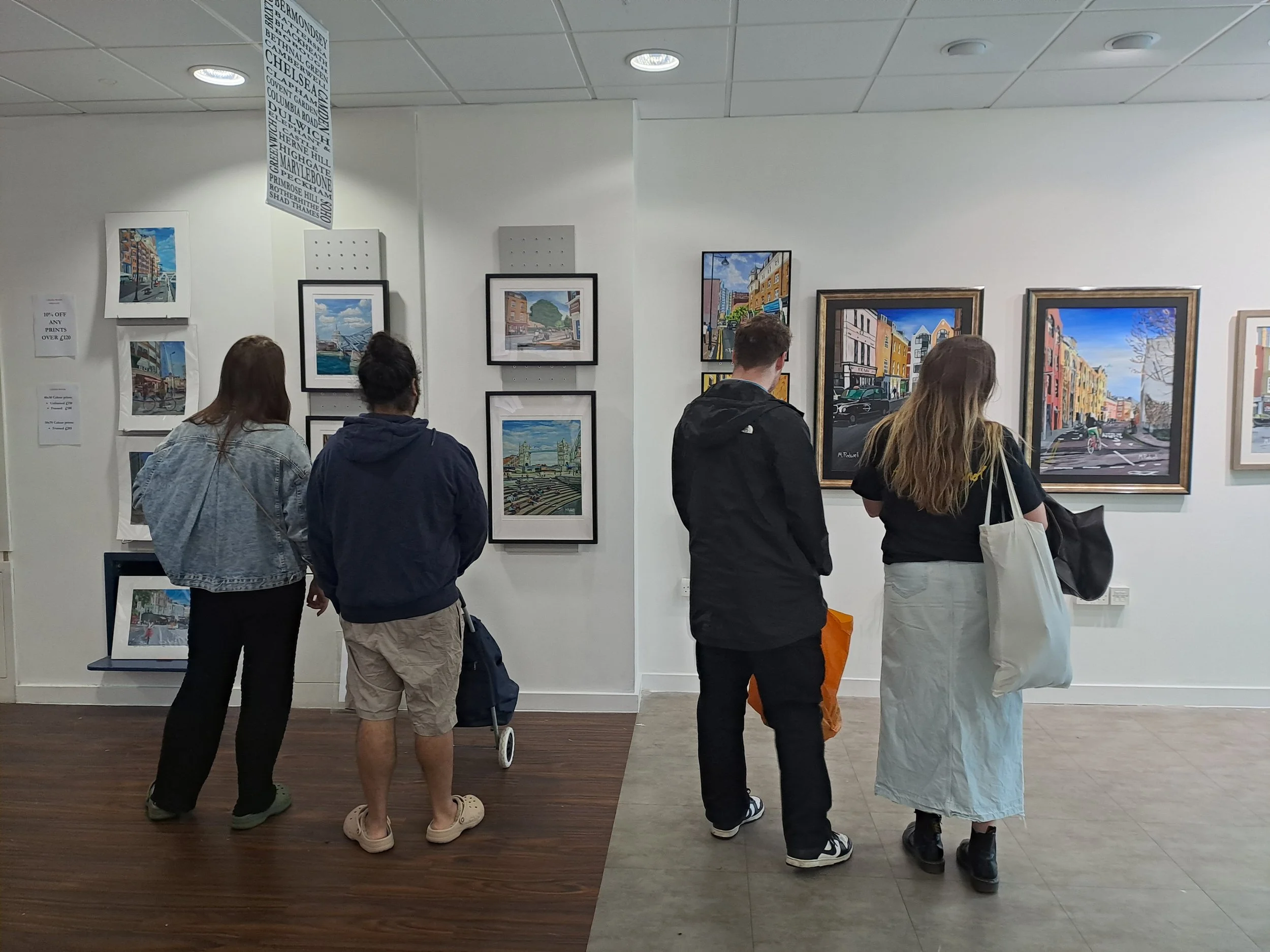 Art lovers admiring prints and original paintings on display at Hidden London.  Artwork by Magnus Rodwell displayed available admire and buy.