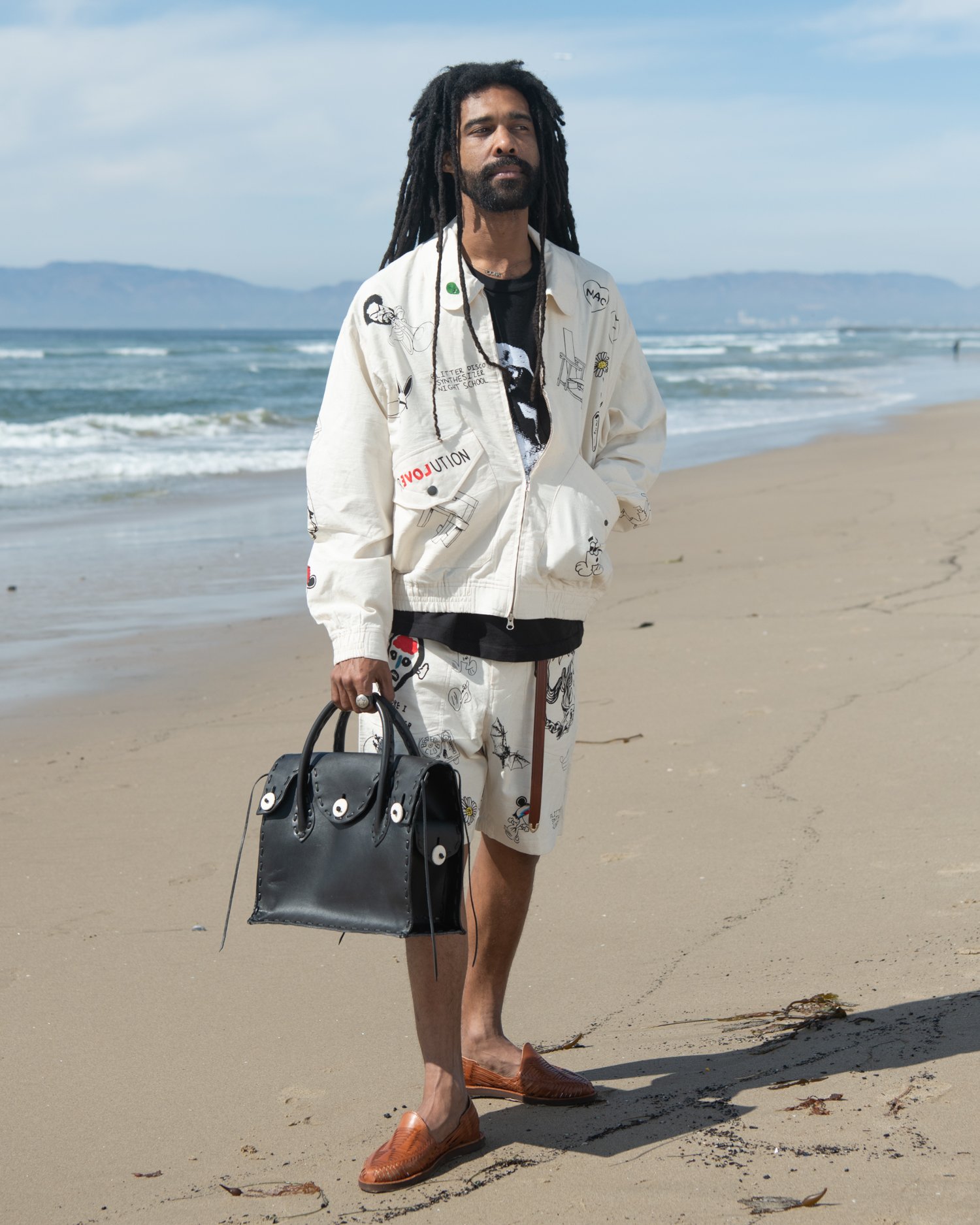 KARDO x JACOB WILDER x MONITALY collaboration hand woven Flight jacket worn by man standing at beach holding Chamula handbag
