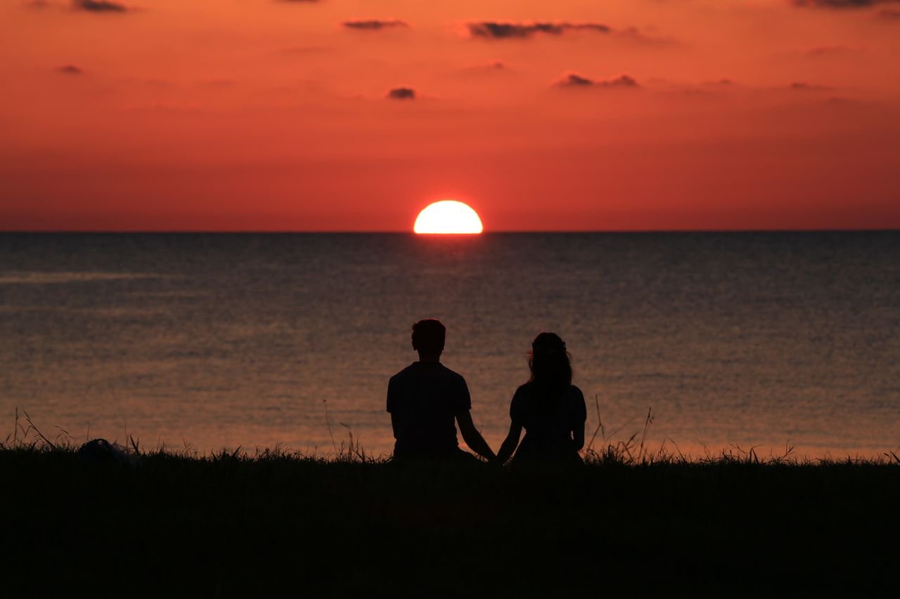 A couple sitting together  watching a vibrant orange sunset over the water