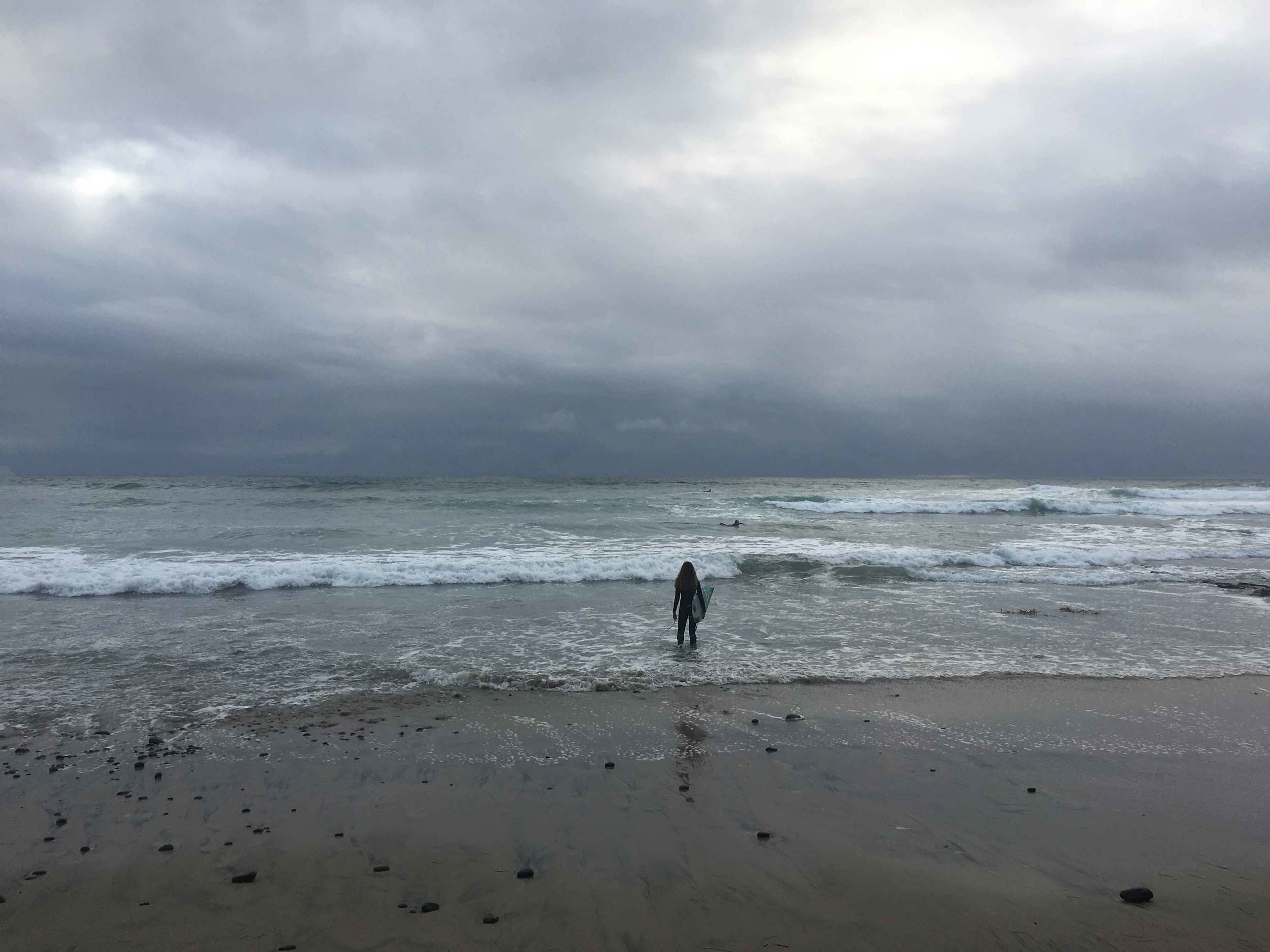 Surfer standing in the ocean, surfer with surfboard, stormy day at the ocean, Swamis beach, Encinitas, California. Image©sourcingstyle.com