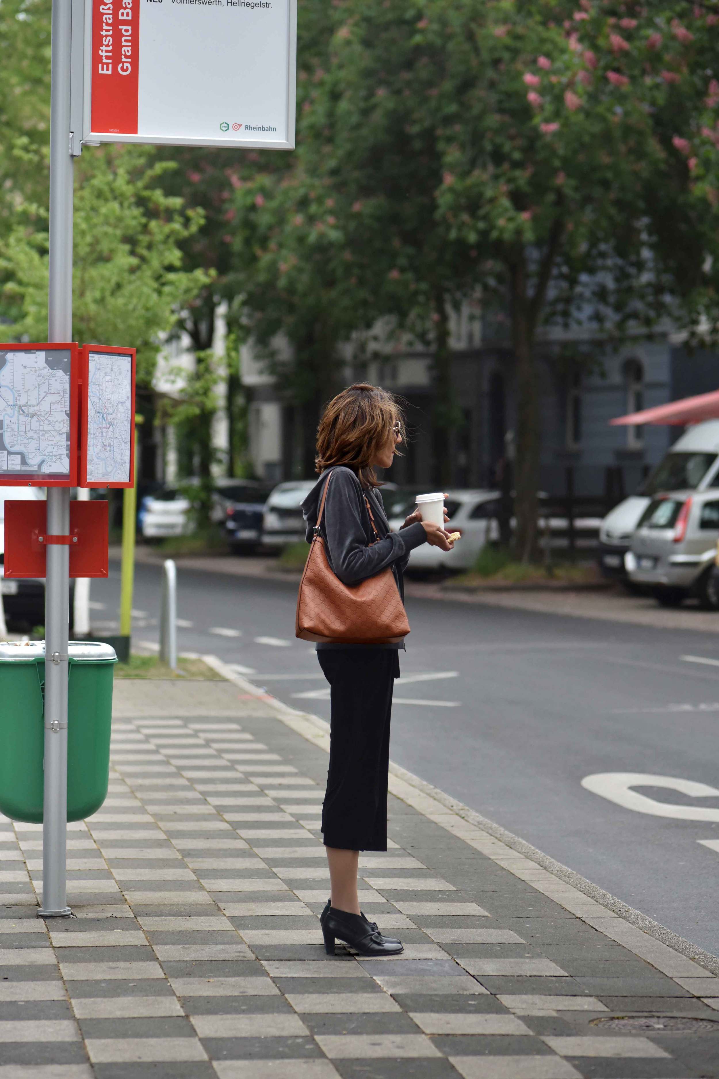 At the bus stop. Wearing Eileen Fisher black tank dress in viscose jersey, little black dress, Gucci handbag, Eddie Bauer velour jacket, Düsseldorf city, Germany. Image©sourcingstyle.com, Photo: Nicola Nolting.