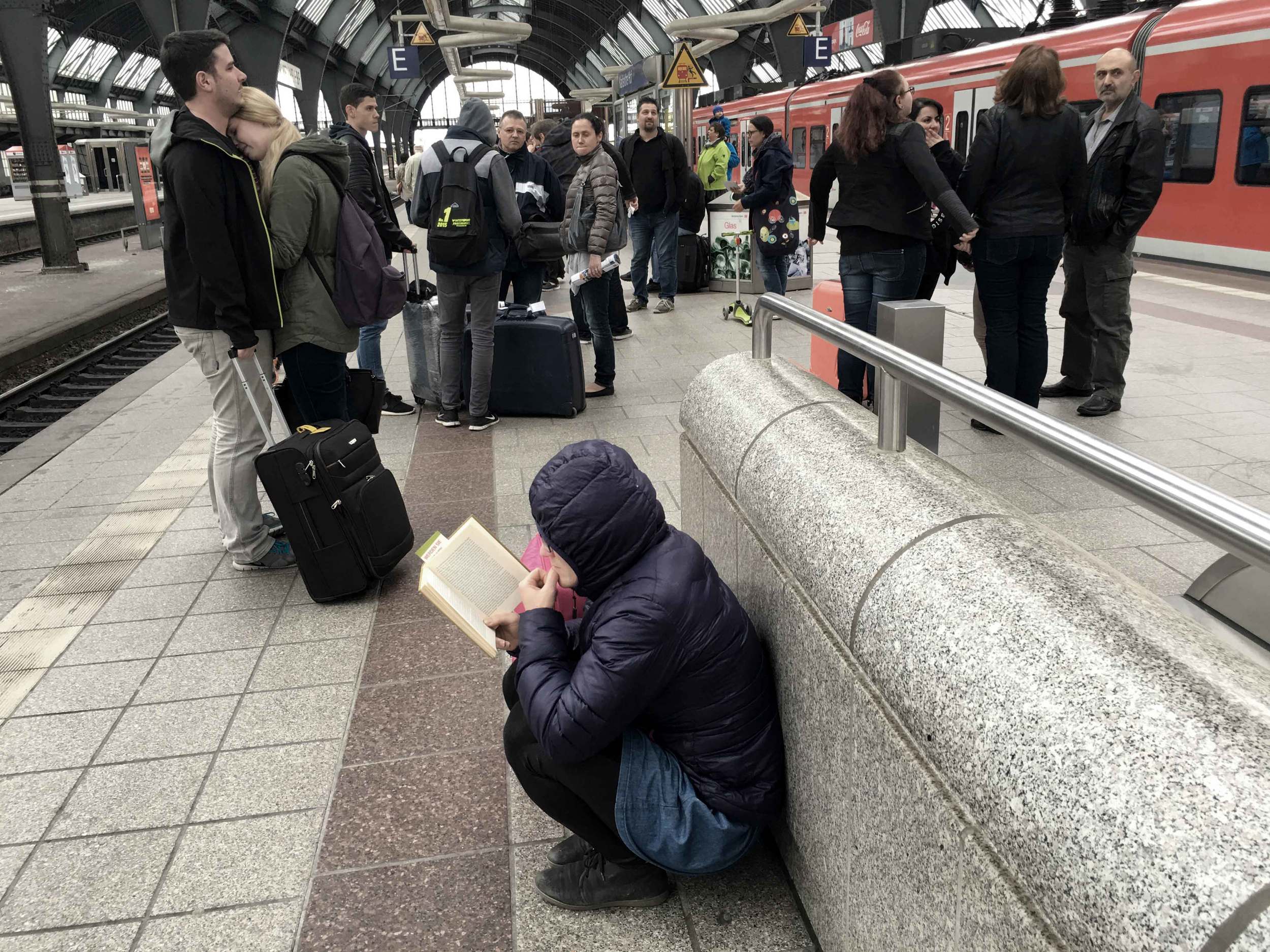 A platform in Germany, Karlsruhe railway station, girl reading a book on the platform, a couple hug and say goodby on the platform. Image©sourcingstyle.com