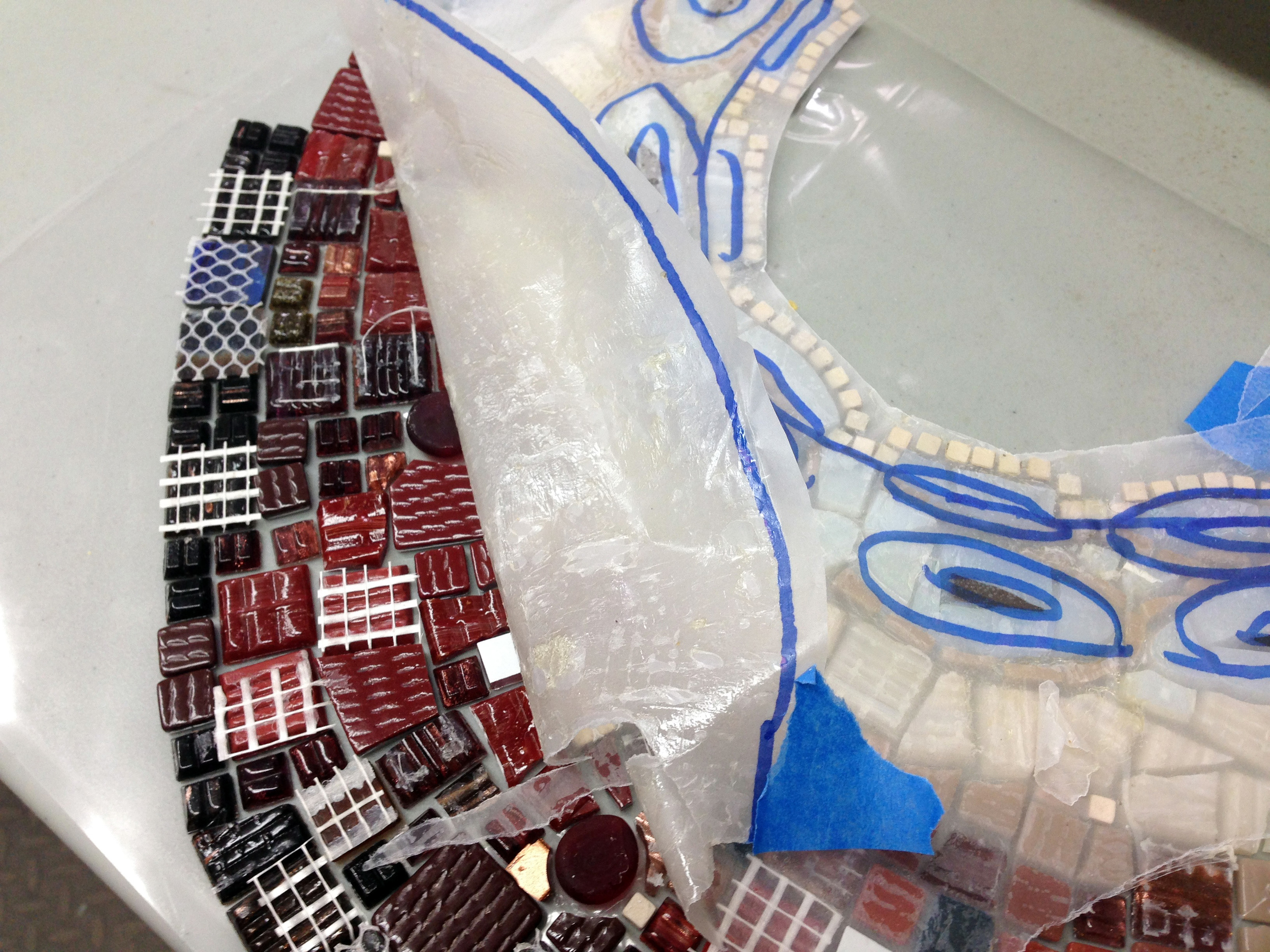 Peeling the tracing paper off the leg section, to leave the tiles in place, but now face down on the contact paper. The white mesh on some of the tile backs indicates which tiles came in the large sheets that I cut up. The ones with no backing (mostly) came loose.