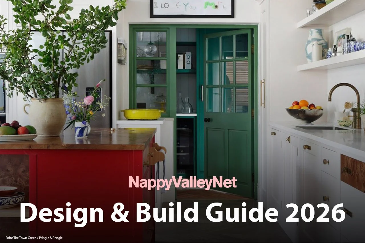 A colorful kitchen with a wooden island, a large potted plant, and shelves with decorative items and dishes. A framed sign hangs above a corner pass-through with green doors leading to another room.