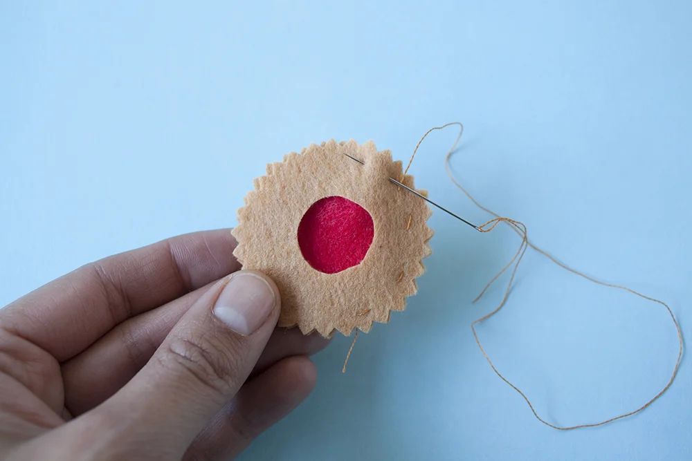 Step 3 Sandwich the red circle between the two brown ones. Using a single strand of light brown embroidery thread, sew all the way around the edge of the biscuit as well as around the inner circle with a simple running stitch.
