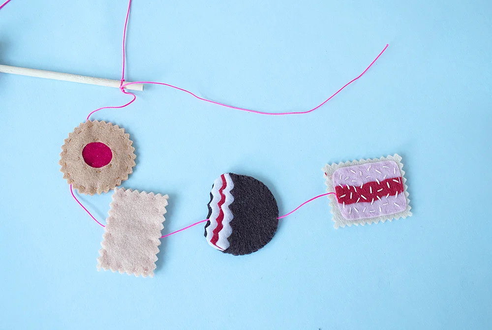 Step 15 Cut two 50cm strands and one 60cm strand of coloured yarn. Thread four assorted biscuits onto each strand, gently manoeuvring the yarn in between the layers of each biscuit (as if you were threading a bead). Use the large-eyed needle for this. To complete your mobile, tie the two 50cm strands onto the edges of the dowel rod and the 60cm strand in the centre.