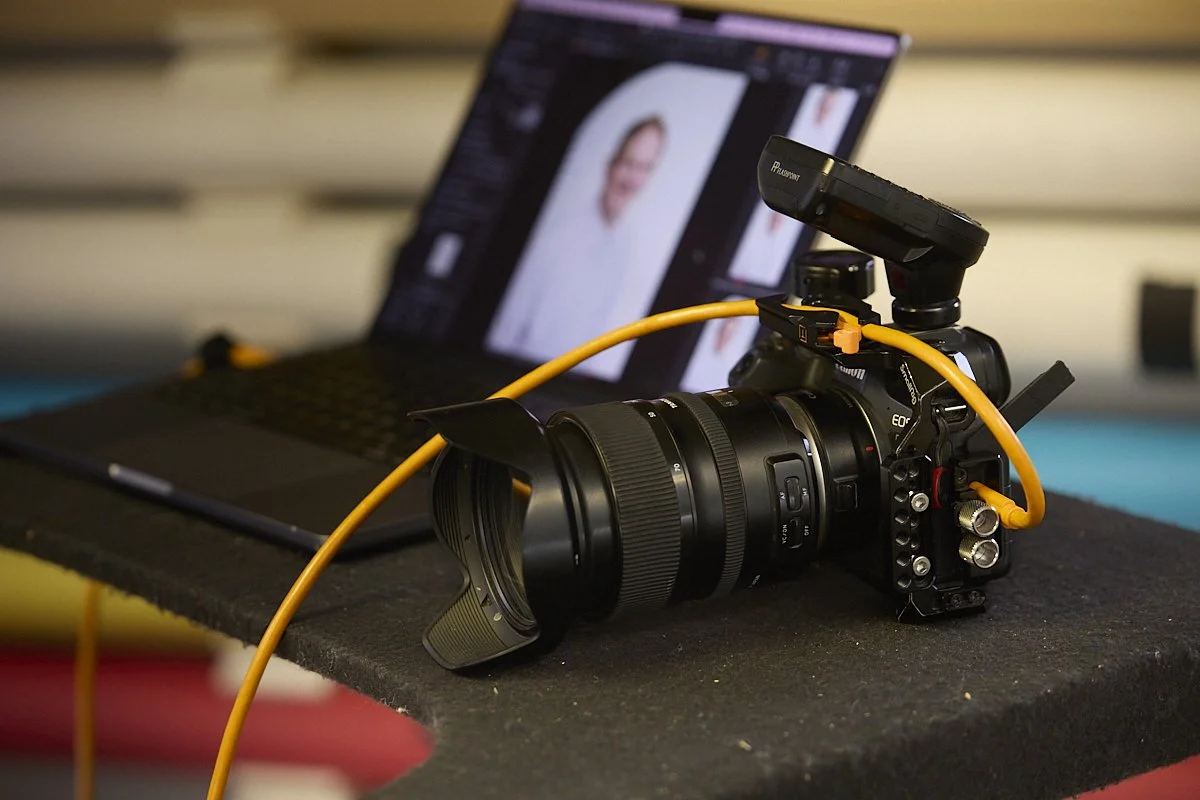 Image of a camera tethered to a computer with a client reviewing their headshots