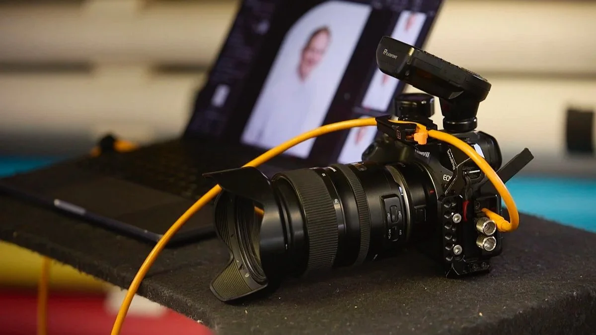 Camera connected to a laptop with a blurred photo editing software open on the screen.