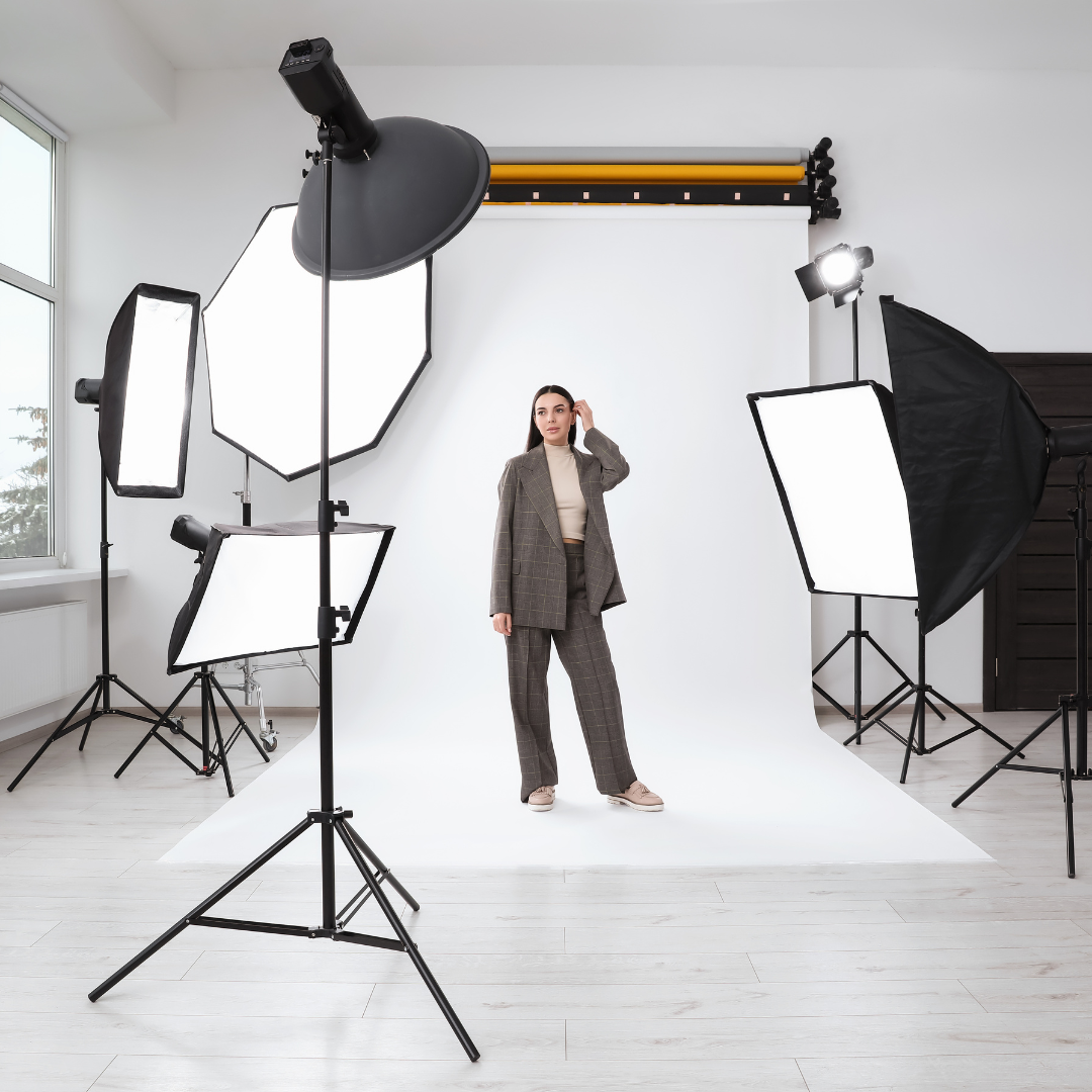 A woman in a checkered suit poses confidently in a well-lit photo studio with multiple softbox lights and a white backdrop.