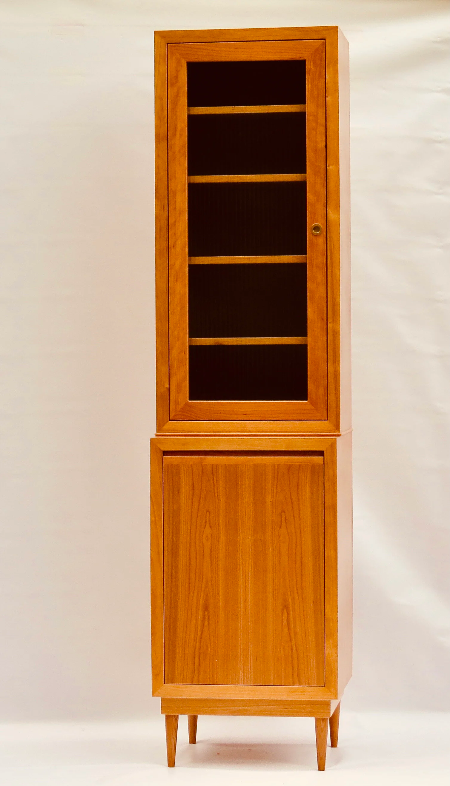 A tall wooden cabinet with a glass door on the upper section, four shelves inside, and a solid door on the lower section, standing on four angled legs.