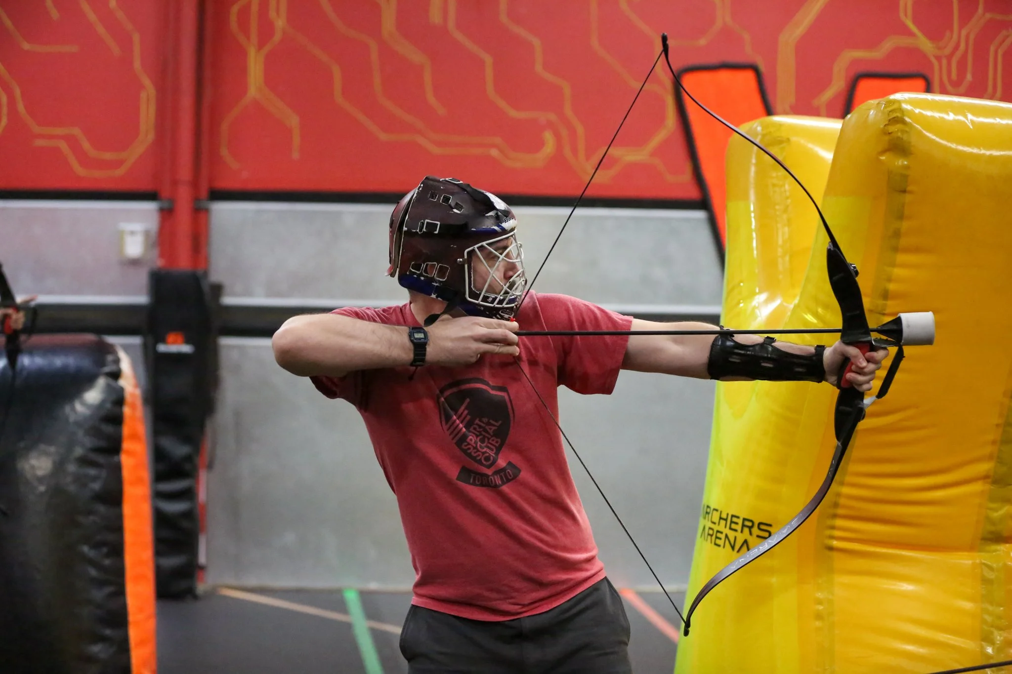 Adults playing combat archery in Toronto arena laughing and dodging arrows